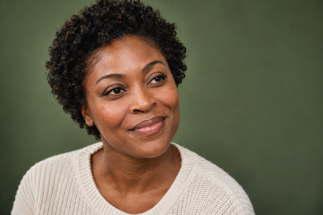 Woman with short natural curls smiling gently against a muted green background.